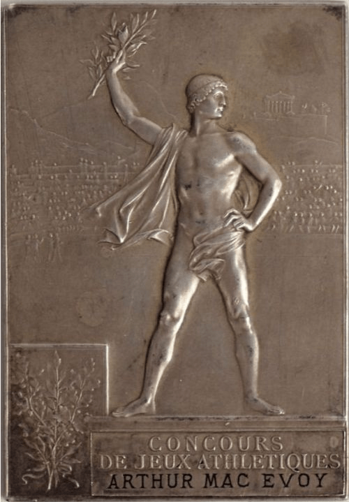 A vintage silver medal featuring a muscular man holding a laurel branch, standing in a dynamic pose, with an ancient Greek cityscape in the background and text reading 'Concours de jeux athlétiques' and 'Arthur Mac Evoy' at the bottom.